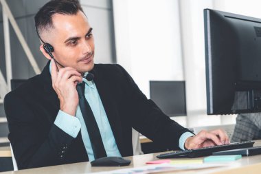 Ofiste çalışan kulaklık takan işadamları uzak müşteri ya da meslektaşlarını desteklemek için çalışıyorlar. Arama merkezi, tele pazarlama, müşteri destek acentesi telefon görüşmesinde hizmet sunar.