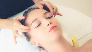 Lüks bir spa merkezinde masaj terapisti tarafından yüz masajı ve spa tedavisi için kaplıcaya uzanmış rahat bir kadın. Sağlık, stres atma ve gençleştirme kavramı.