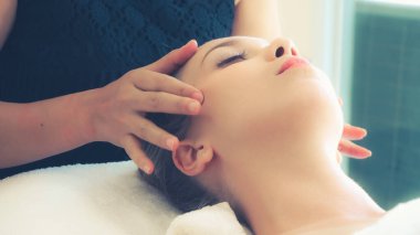 Lüks bir spa merkezinde masaj terapisti tarafından yüz masajı ve spa tedavisi için kaplıcaya uzanmış rahat bir kadın. Sağlık, stres atma ve gençleştirme kavramı.