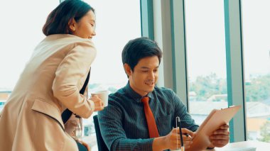 İki iş adamı toplantı odasında proje stratejisi hakkında konuşuyor. İş adamı, mali veri raporu hakkında sohbet ve tavsiyelerde bulunurken, modern işyerindeki iş arkadaşıyla proje planlamasını tartıştı.