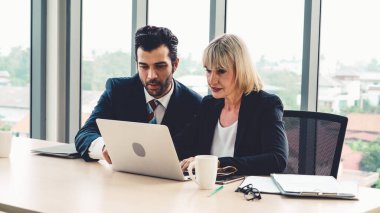 İki iş adamı toplantı odasında proje stratejisi hakkında konuşuyor. İş adamı, mali veri raporu hakkında sohbet ve tavsiyelerde bulunurken, modern işyerindeki iş arkadaşıyla proje planlamasını tartıştı.