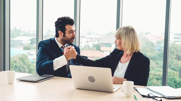 Two happy business people celebrate at office meeting room. Successful businessman congratulate project success with colleague at modern workplace while having conversation on financial data report.