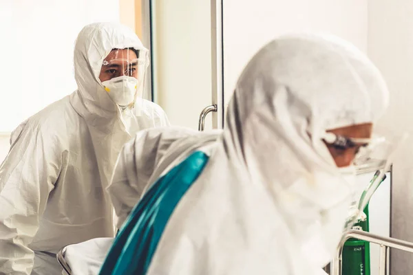 Emergency medic and doctor moving patient to emergency room in hospital . Doctor wears protective suit and face mask in concept of coronavirus and covid 19 protection and quarantine .
