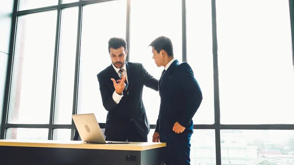 Two business people talk project strategy at office meeting room. Businessman discuss project planning with colleague at modern workplace while having conversation and advice on financial data report.