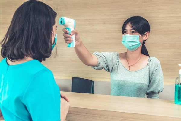 Receptionist and guest wearing face mask at front desk while having conversation in office or hospital . Covid 19 and coronavirus infection protection and protective policy concept .