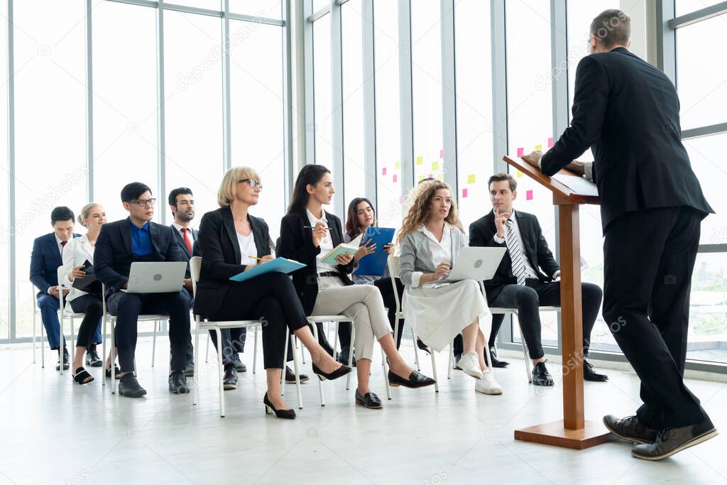 Group of business people meeting in a seminar conference . Audience listening to instructor in employee education training session . Office worker community summit forum with expert speaker .