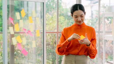 İş adamları ofisteki proje planlama kurulunda çalışıyor ve proje gelişimini analiz etmek için iş arkadaşlarıyla sohbet ediyorlar. Düzenli olması için cam duvara yapıştırılmış yapışkan notlar kullanıyorlar. .