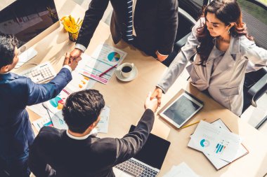 Grup iş adamları toplantı masasında el sıkışırken üst açıdan kendilerine güvenirler. Genç işadamı ve işkadını işçiler yatırım anlaşması imzaladılar.