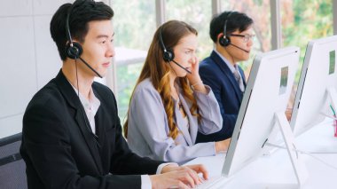 Ofiste çalışan kulaklık takan işadamları uzak müşteri ya da meslektaşlarını desteklemek için çalışıyorlar. Arama merkezi, tele pazarlama, müşteri destek acentesi telefon görüşmesinde hizmet sunar.