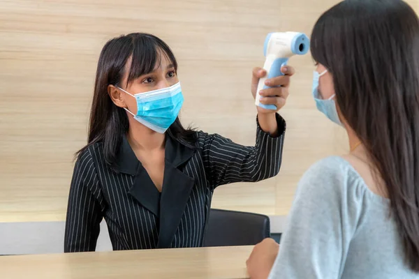 Receptionist and guest wearing face mask at front desk while having conversation in office or hospital . Covid 19 and coronavirus infection protection and protective policy concept .