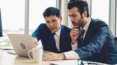 İki iş adamı toplantı odasında proje stratejisi hakkında konuşuyor. İş adamı, mali veri raporu hakkında sohbet ve tavsiyelerde bulunurken, modern işyerindeki iş arkadaşıyla proje planlamasını tartıştı.