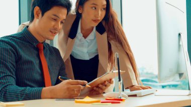 İki iş adamı toplantı odasında proje stratejisi hakkında konuşuyor. İş adamı, mali veri raporu hakkında sohbet ve tavsiyelerde bulunurken, modern işyerindeki iş arkadaşıyla proje planlamasını tartıştı.