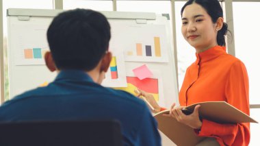Genç bir kadın günlük ofis odasındaki beyaz tahtadaki iş verilerini açıklıyor. Kendine güvenen Asyalı işkadını, pazar stratejisini belirlemek için ortak olarak yürütülen bir iş projesinin bilgi ilerlemesini rapor etti .