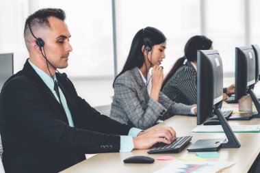 Ofiste çalışan kulaklık takan işadamları uzak müşteri ya da meslektaşlarını desteklemek için çalışıyorlar. Arama merkezi, tele pazarlama, müşteri destek acentesi telefon görüşmesinde hizmet sunar.