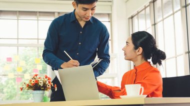 İki iş adamı toplantı odasında proje stratejisi hakkında konuşuyor. İş adamı, mali veri raporu hakkında sohbet ve tavsiyelerde bulunurken, modern işyerindeki iş arkadaşıyla proje planlamasını tartıştı.