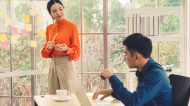 İş adamları ofisteki proje planlama kurulunda çalışıyor ve proje gelişimini analiz etmek için iş arkadaşlarıyla sohbet ediyorlar. Düzenli olması için cam duvara yapıştırılmış yapışkan notlar kullanıyorlar. .