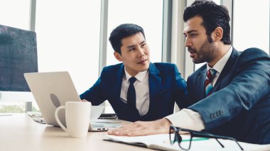 İki iş adamı toplantı odasında proje stratejisi hakkında konuşuyor. İş adamı, mali veri raporu hakkında sohbet ve tavsiyelerde bulunurken, modern işyerindeki iş arkadaşıyla proje planlamasını tartıştı.