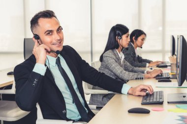 Ofiste çalışan kulaklık takan işadamları uzak müşteri ya da meslektaşlarını desteklemek için çalışıyorlar. Arama merkezi, tele pazarlama, müşteri destek acentesi telefon görüşmesinde hizmet sunar.