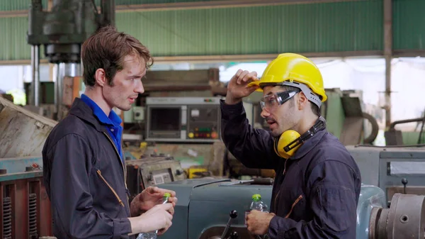 Tired factory workers taking a break and talking to coworker in the factory . Industry and engineering concept .