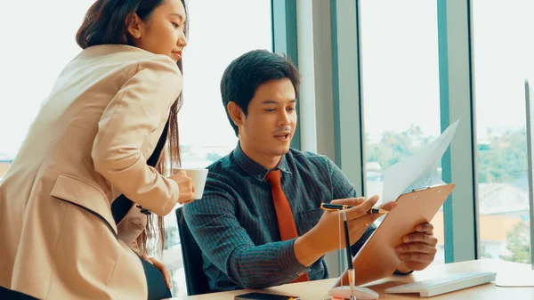 İki iş adamı toplantı odasında proje stratejisi hakkında konuşuyor. İş adamı, mali veri raporu hakkında sohbet ve tavsiyelerde bulunurken, modern işyerindeki iş arkadaşıyla proje planlamasını tartıştı.