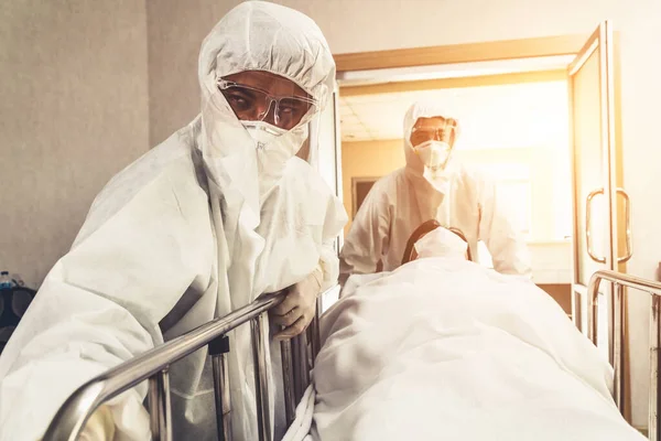 Emergency medic and doctor moving patient to emergency room in hospital . Doctor wears protective suit and face mask in concept of coronavirus and covid 19 protection and quarantine .
