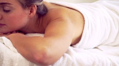 Rahatlamış genç bir kadın masaj için spa yatağında yatıyor..