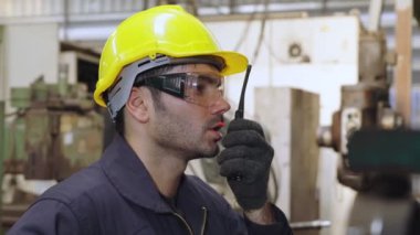 Fabrika işçisi, makine parçalarını incelerken taşınabilir radyodan konuşuyor.