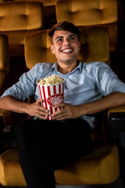 Genç bir adam sinemada film izlerken patlamış mısırla eğleniyor.