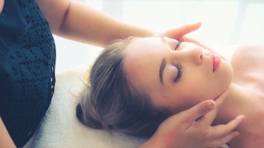 Lüks bir spa merkezinde masaj terapisti tarafından yüz masajı ve spa tedavisi için kaplıcaya uzanmış rahat bir kadın. Sağlık, stres atma ve gençleştirme kavramı.