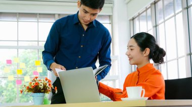 İki iş adamı toplantı odasında proje stratejisi hakkında konuşuyor. İş adamı, mali veri raporu hakkında sohbet ve tavsiyelerde bulunurken, modern işyerindeki iş arkadaşıyla proje planlamasını tartıştı.