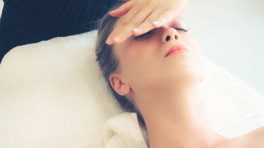 Lüks bir spa merkezinde masaj terapisti tarafından yüz masajı ve spa tedavisi için kaplıcaya uzanmış rahat bir kadın. Sağlık, stres atma ve gençleştirme kavramı.