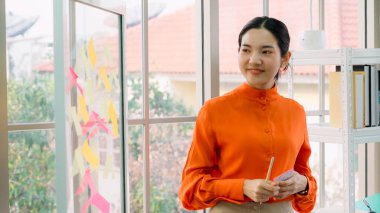 İş adamları ofisteki proje planlama kurulunda çalışıyor ve proje gelişimini analiz etmek için iş arkadaşlarıyla sohbet ediyorlar. Düzenli olması için cam duvara yapıştırılmış yapışkan notlar kullanıyorlar. .