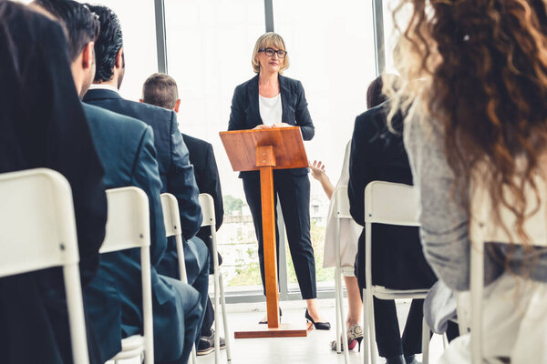 Group of business people meeting in a seminar conference . Audience listening to instructor in employee education training session . Office worker community summit forum with expert speaker .