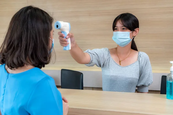 Receptionist and guest wearing face mask at front desk while having conversation in office or hospital . Covid 19 and coronavirus infection protection and protective policy concept .