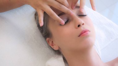 Lüks bir spa merkezinde masaj terapisti tarafından yüz masajı ve spa tedavisi için kaplıcaya uzanmış rahat bir kadın. Sağlık, stres atma ve gençleştirme kavramı.