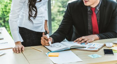 İki iş adamı toplantı odasında proje stratejisi hakkında konuşuyor. İş adamı, mali veri raporu hakkında sohbet ve tavsiyelerde bulunurken, modern işyerindeki iş arkadaşıyla proje planlamasını tartıştı.