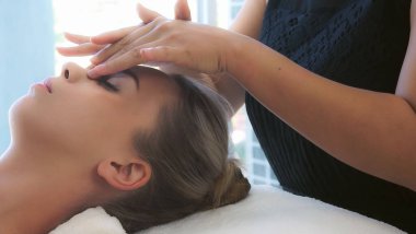 Lüks bir spa merkezinde masaj terapisti tarafından yüz masajı ve spa tedavisi için kaplıcaya uzanmış rahat bir kadın. Sağlık, stres atma ve gençleştirme kavramı.