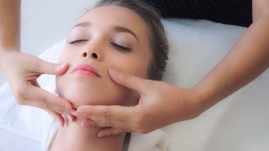 Lüks bir spa merkezinde masaj terapisti tarafından yüz masajı ve spa tedavisi için kaplıcaya uzanmış rahat bir kadın. Sağlık, stres atma ve gençleştirme kavramı.