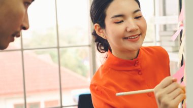 İş adamları ofisteki proje planlama kurulunda çalışıyor ve proje gelişimini analiz etmek için iş arkadaşlarıyla sohbet ediyorlar. Düzenli olması için cam duvara yapıştırılmış yapışkan notlar kullanıyorlar. .