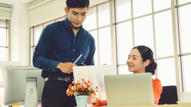 İki iş adamı toplantı odasında proje stratejisi hakkında konuşuyor. İş adamı, mali veri raporu hakkında sohbet ve tavsiyelerde bulunurken, modern işyerindeki iş arkadaşıyla proje planlamasını tartıştı.