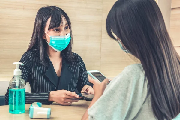 Receptionist and guest wearing face mask at front desk while having conversation in office or hospital . Covid 19 and coronavirus infection protection and protective policy concept .