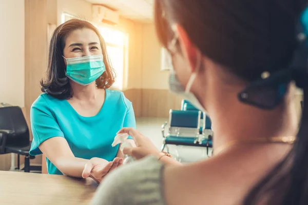 Receptionist and guest wearing face mask at front desk while having conversation in office or hospital . Covid 19 and coronavirus infection protection and protective policy concept .
