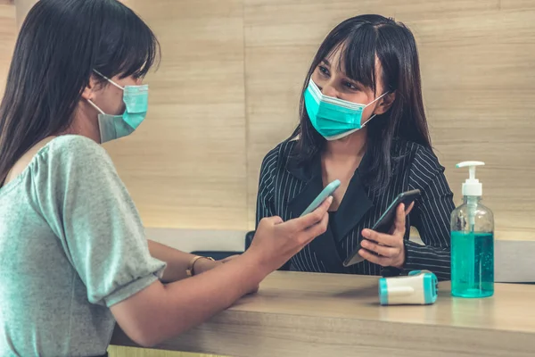 Receptionist and guest wearing face mask at front desk while having conversation in office or hospital . Covid 19 and coronavirus infection protection and protective policy concept .