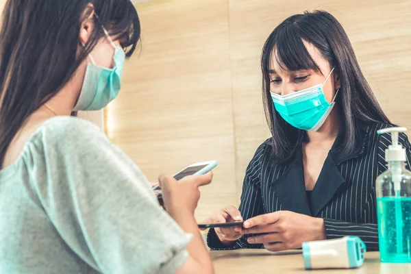 Receptionist and guest wearing face mask at front desk while having conversation in office or hospital . Covid 19 and coronavirus infection protection and protective policy concept .