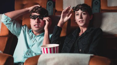 Sinemada üç boyutlu gözlüklü bir kadın ve erkek film izliyor. Ekrana bakar, heyecan verici ve patlamış mısır yer.