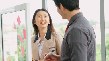 İş adamları ofisteki proje planlama kurulunda çalışıyor ve proje gelişimini analiz etmek için iş arkadaşlarıyla sohbet ediyorlar. Düzenli olması için cam duvara yapıştırılmış yapışkan notlar kullanıyorlar. .