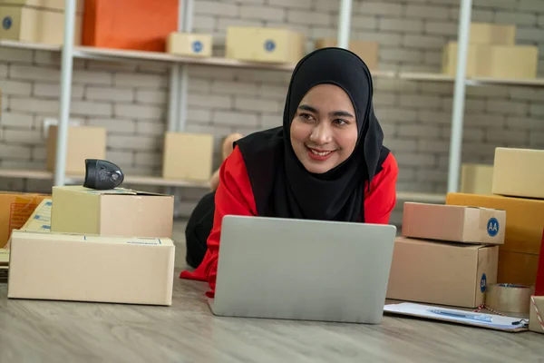 Muslim online seller at home office with shipping box for delivery to customer. Small business owner or entrepreneur doing e-commerce business on the internet.