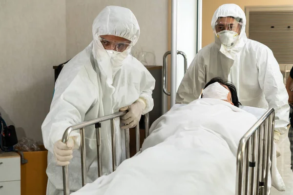 Emergency medic and doctor moving patient to emergency room in hospital . Doctor wears protective suit and face mask in concept of coronavirus and covid 19 protection and quarantine .