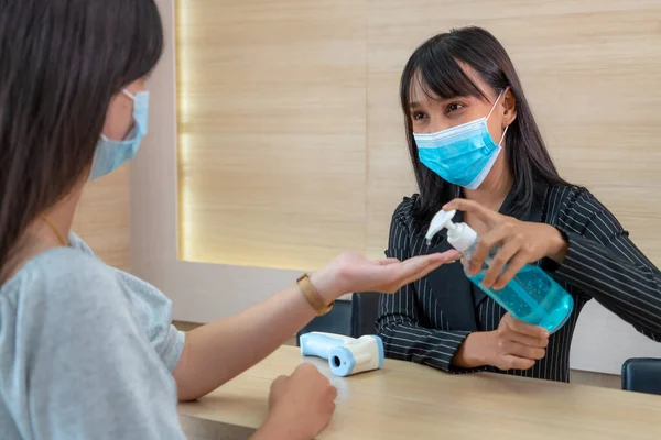 Receptionist and guest wearing face mask at front desk while having conversation in office or hospital . Covid 19 and coronavirus infection protection and protective policy concept .