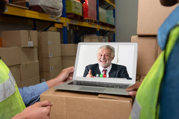 Warehouse staff talking on video call at computer screen in storage warehouse